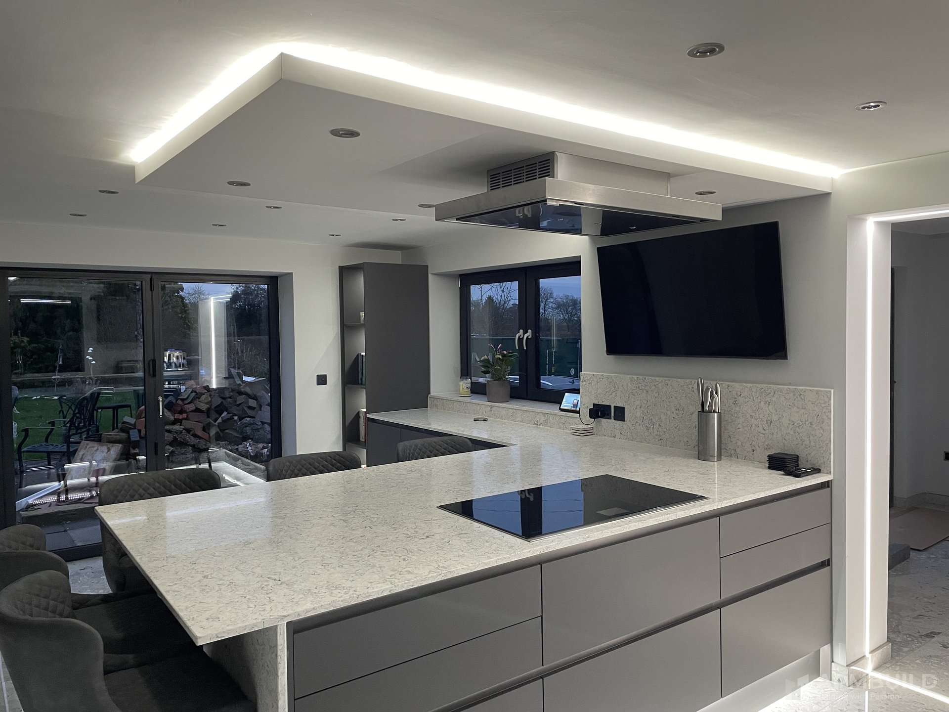 Open-plan kitchen with quartz island, statement hood, and LED-cove ceiling in a Gorsley home by APMBuild, Herefordshire